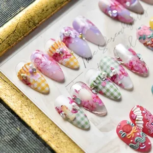Artistic press-on nail set featuring pink floral patterns, lace motifs, and 3D pearls