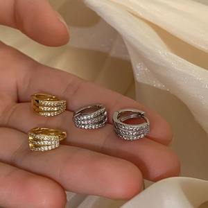 Elegant gold and silver pavé zircon huggie hoop earrings on a soft cream silk fabric