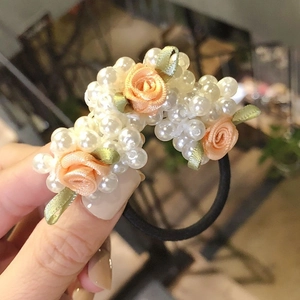 Detail of handmade hair tie featuring orange fabric rose, white pearls and green ribbon