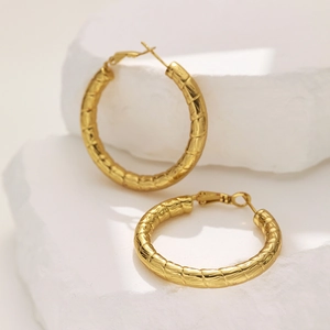 Detail view of gold hoop earrings with segmented bamboo texture on a white stone background