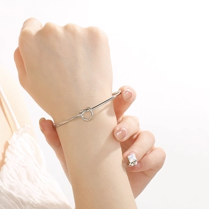 Close-up of minimalist silver knot cuff bracelet worn on wrist showing sleek metallic texture