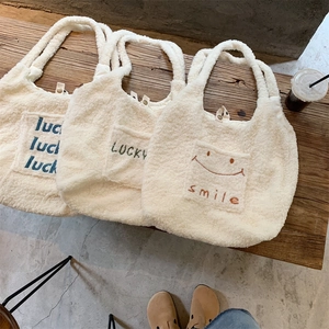 Close-up of three beige plush fleece tote bags with letter embroidery on a vintage bench