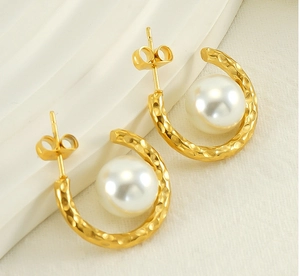 Détail de boucles d'oreilles dorées en C avec texture martelée et grosse perle