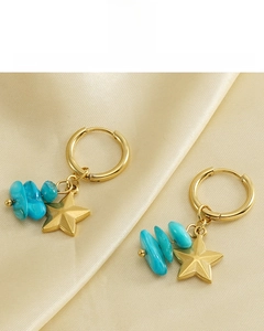 Detail of 18k gold plated star earrings with blue turquoise stones on satin fabric