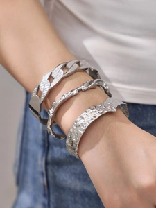 Detail view of silver metal bangles featuring heavy hammered textures and chunky chain links