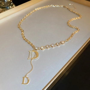 Detailed macro view of gold Y-necklace with crystal pavé D pendants on a beige tray