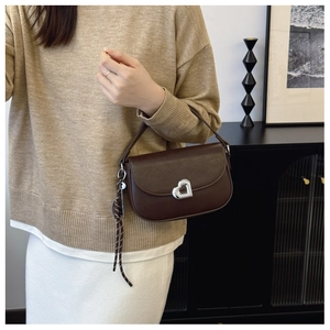 Detail of dark brown leather handbag featuring silver heart clasp and woven charm knot