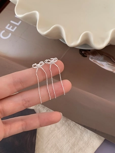 Detail of silver bow tassel earrings held by hand over a minimalist white ceramic tray
