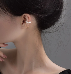 Detail of gold-plated ear cuff with small white pearls and elegant hanging chains on ear