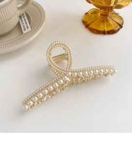 Vue détaillée d'une grande pince à cheveux en métal doré avec perles blanches et strass chic