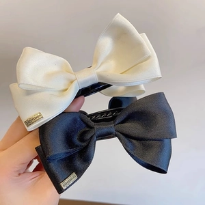 Detail view of large satin bow hair clips in black and white with metal logo accents