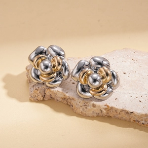 Detail of silver and gold flower studs on beige stone showcasing dual-tone metal texture