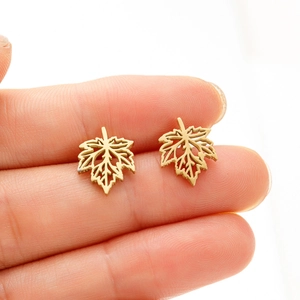 Boucles d'oreilles feuilles d'érable dorées en acier inoxydable sur le bout du doigt