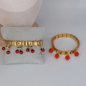 Italian style gold stretch bracelet set with red strawberry and cherry charms on grey pillow