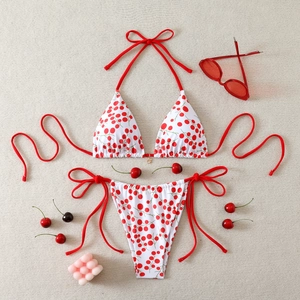 Flat lay of cherry print bikini with red ties, sunglasses and fresh cherries on beige