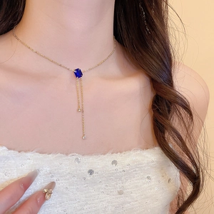 Detail of gold necklace with deep blue rectangular gemstone and dual metallic tassels
