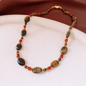 Détail du collier en œil de tigre plaqué or 18k avec perles rouges sur assiette