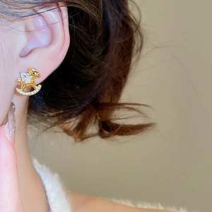 Close-up of gold-plated rocking horse earring with pear-cut zircon on female ear