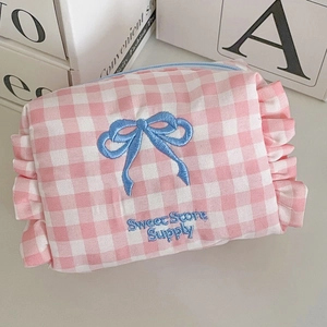 Pink plaid cosmetic bag with blue bow embroidery and ruffled edges on light background