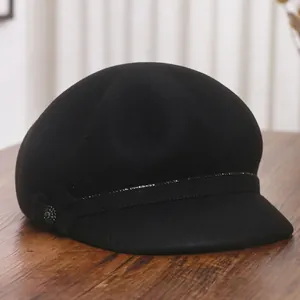 Elegant black wool octagonal newsboy hat with bow and gemstone detail on wooden surface