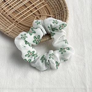 Close-up of floral fabric scrunchie with green petals on a rustic woven tray