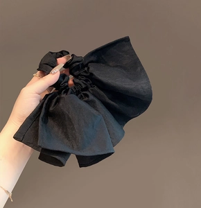 Detail of a large black fabric bow scrunchie held in hand to show size and satin texture
