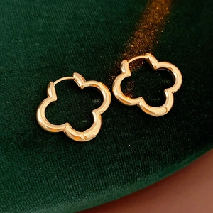Detailed close-up of golden hollow clover hoop earrings on green velvet background