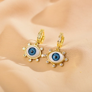 Detail of gold evil eye earrings with blue inlay and white rhinestones on pink fabric