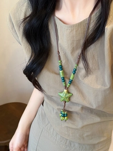 Detail of green ceramic starfish pendant and beads on dark brown woven sweater chain