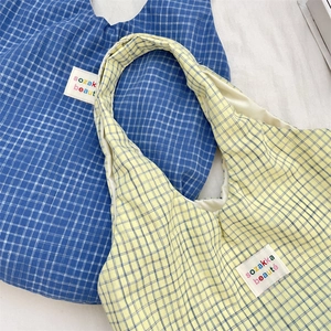 Detail of blue and yellow plaid canvas tote bags with woven label on plain fabric background