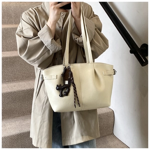 Detail of cream pleated tote bag with cat charm and woven strap on a model