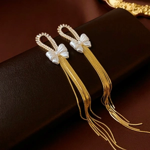 Close-up of elegant gold tassel earrings with white bow detail and shimmering crystals