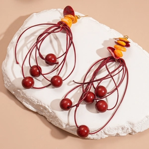 Bohemian oversized earrings with red beads and orange shell accents on stone display