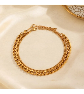 Detail of gold layered Cuban link anklet with lobster clasp on beige silk fabric background