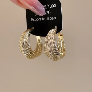 Detail showing gold multi-layered C-shaped earrings with rich woven texture and metallic luster