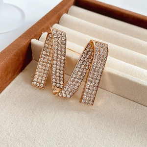 Close-up of a sparkling gold letter M brooch with crystal inlay on a beige jewelry box