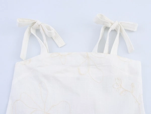 Detail des weißen Tops mit blassgelber Blumenstickerei und Schleifen an den Trägern