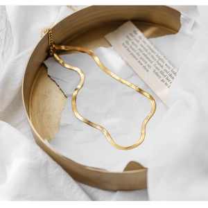 Detail of a thin gold snake bone chain necklace displayed on a golden metal tray