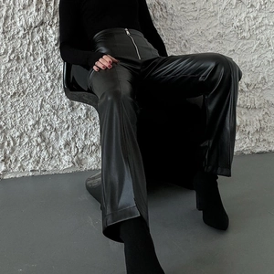 Detail shot of high-waisted black PU leather trousers featuring a metallic front zipper