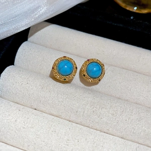 Macro shot of vintage round gold earrings with turquoise center on beige velvet
