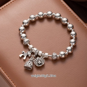 Silver beaded bracelet with charms like a horse and lucky bag shown on leather box