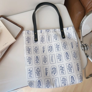 Detail of canvas tote bag featuring blue floral print and black leather handles with rivets