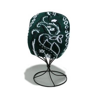 Détail du bonnet en tricot vert foncé avec motifs paisley blancs sur support métal