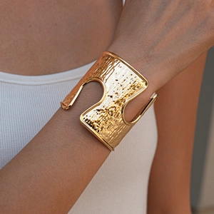 Close-up of golden wide cuff bracelet featuring hollow cut-outs and hammered texture metal