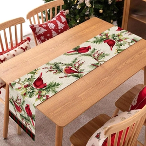 Christmas table runner with cardinals and berries on a wooden table near a festive tree