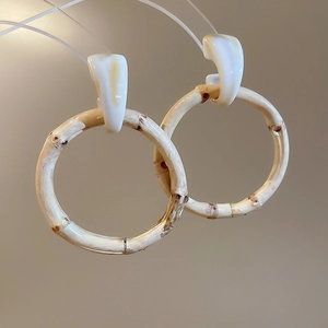 Close-up of bamboo textured hoop earrings with cream resin studs on a khaki background
