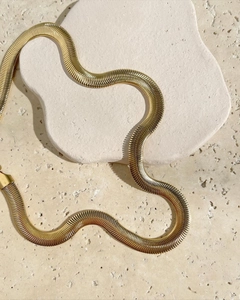 Modern 8mm golden herringbone snake chain necklace laid on stone in natural sunlight