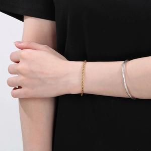 Dettaglio di un bracciale a catena a corda dorata al polso con design minimalista unisex