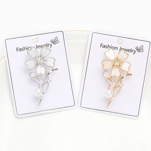 Detailed view of elegant silver and gold flower brooches with faux pearls on display card