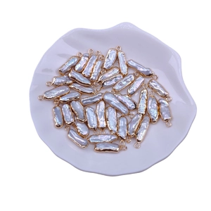 Baroque teardrop pearl charms with gold loops on a ceramic plate for DIY jewelry making